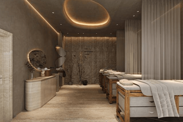 Twin massage beds rest beneath a halo-lit ceiling with warm stone wall, creating an atmosphere of curated calm and privacy.