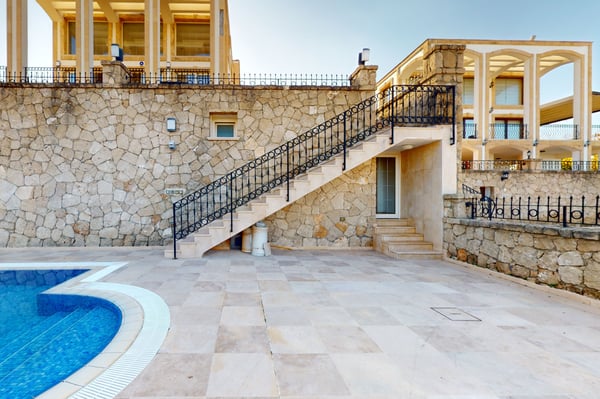 Front facade of the villa with a grand staircase leading up to the main entrance, surrounded by decorative stonework and lush greenery.