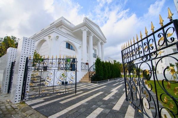 Automatic wrought-iron gate entry framed by a manicured drive and elegant architecture for refined arrival.
