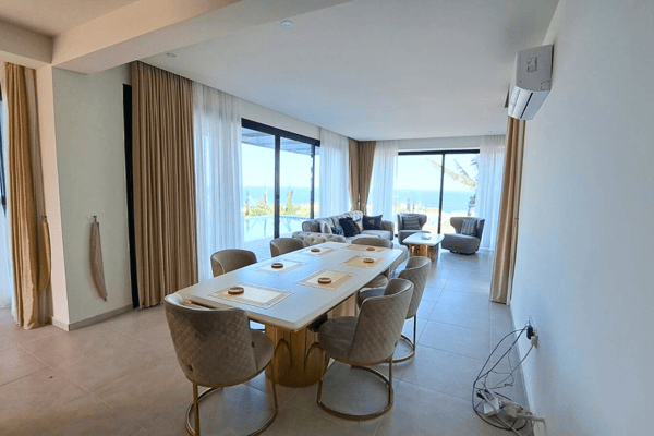 Elegant dining area with plush chairs and glass doors that open to stunning sea views and breezy ambiance.