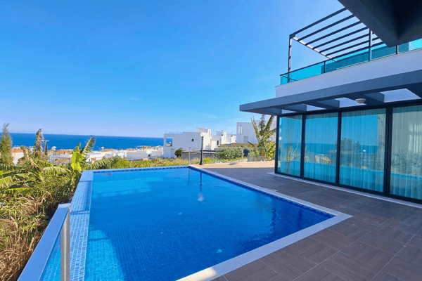 Rear perspective of a villa merging poolside living with uninterrupted ocean views through expansive glass walls.