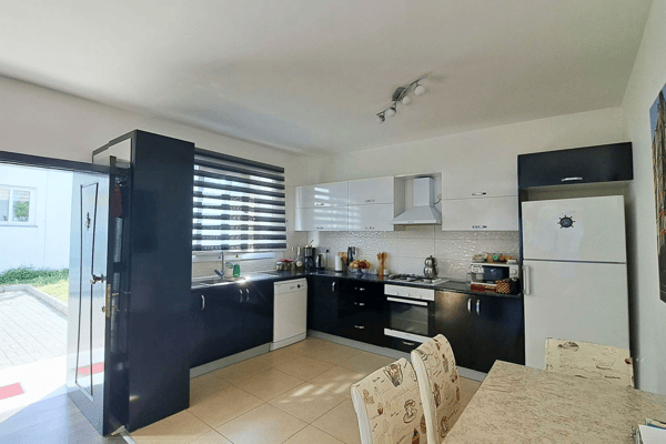Kitchen view towards patio door with garden access, featuring breakfast bar and ample storage for easy alfresco dining.