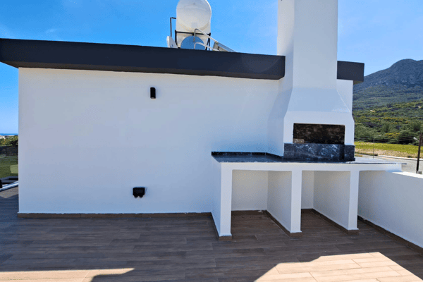 Whitewashed rooftop BBQ setup, surrounded by views of greenery and hills.
