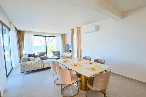 Expanded view of dining and living area with stylish furniture and ocean backdrop, ideal for entertaining.