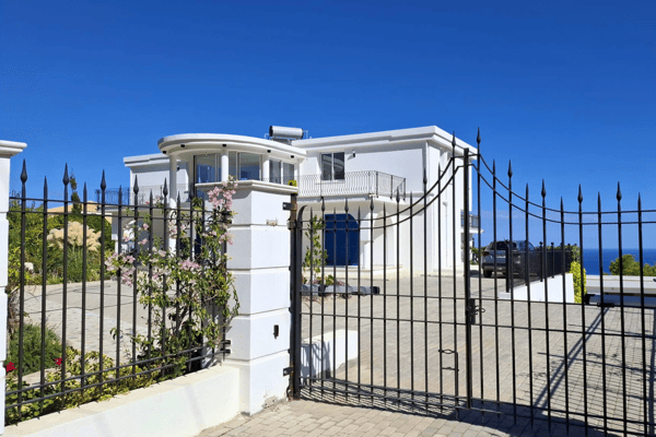 Entry gate with iron bars, stone driveway, and mountain backdrop.