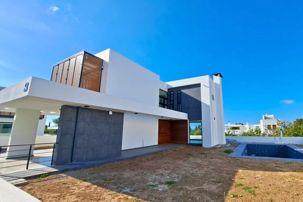 Rear view of a contemporary villa with a private pool and mountain scenery, tiled patio, and clean white exterior under bright skies.