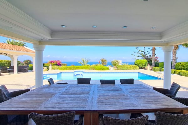 Covered outdoor dining terrace with ten-seat table and glass windbreak, offering uninterrupted views under a timber ceiling.