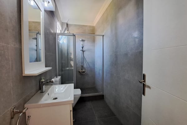 Ensuite bathroom with rain shower and floating vanity, wrapped in grey porcelain for a contemporary sanctuary.