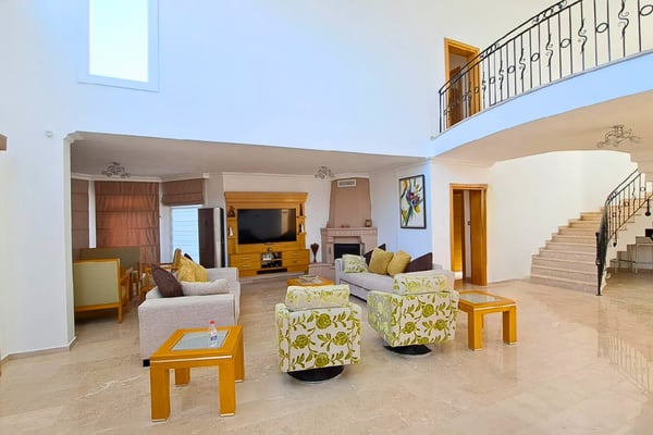 Double-height living room with open stairwell, amplifying space and light while showcasing the villa’s architectural volume.