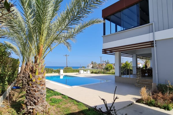 Stylish open-plan living area in a Northern Cyprus villa, with floor-to-ceiling glass doors framing a spectacular sea and pool view.
