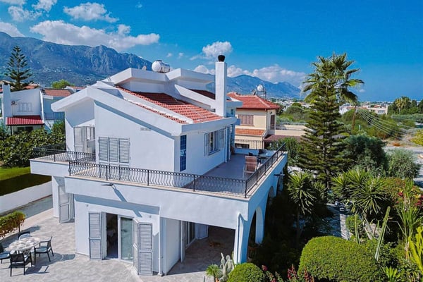 Aerial perspective of a modern white house with a stone yard, revealing a breathtaking view of distant hills and coastline.
