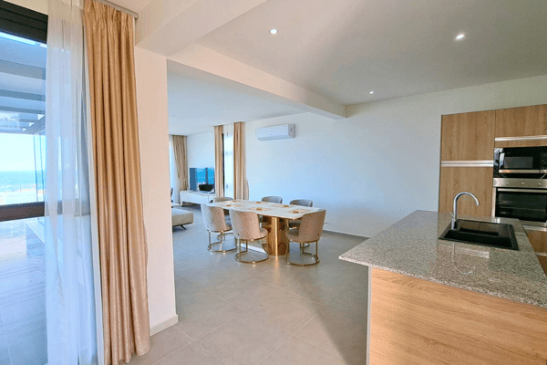 Dining and kitchen blend in an open setting, with curtain-lined windows offering soft light and garden views.