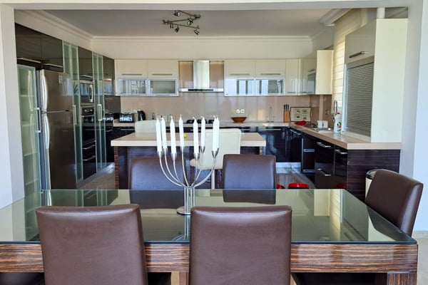 Formal dining room with terrace access and leather seating, where large doors merge indoor space with sea-view living.