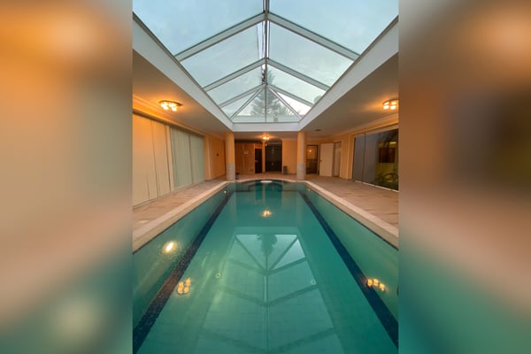 Indoor heated pool enclosed by glass walls, allowing sunlight and relaxation.