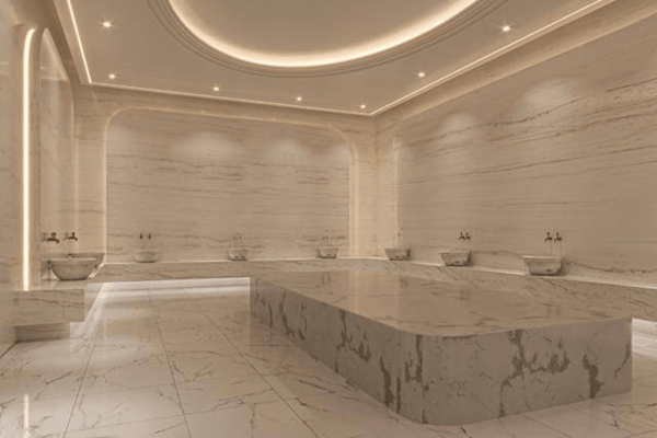 Marble hammam room glows under halo lights with recessed basins and a central heated slab evoking ancient spa traditions.