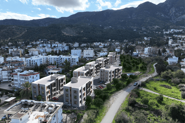 Aerial view capturing the development nestled in green hills with the sea beyond, highlighting a secluded and picturesque residential setting.