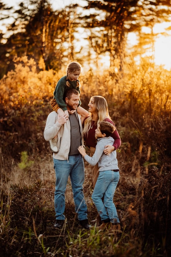 Family of four with little girl on dads shoulders at sunset