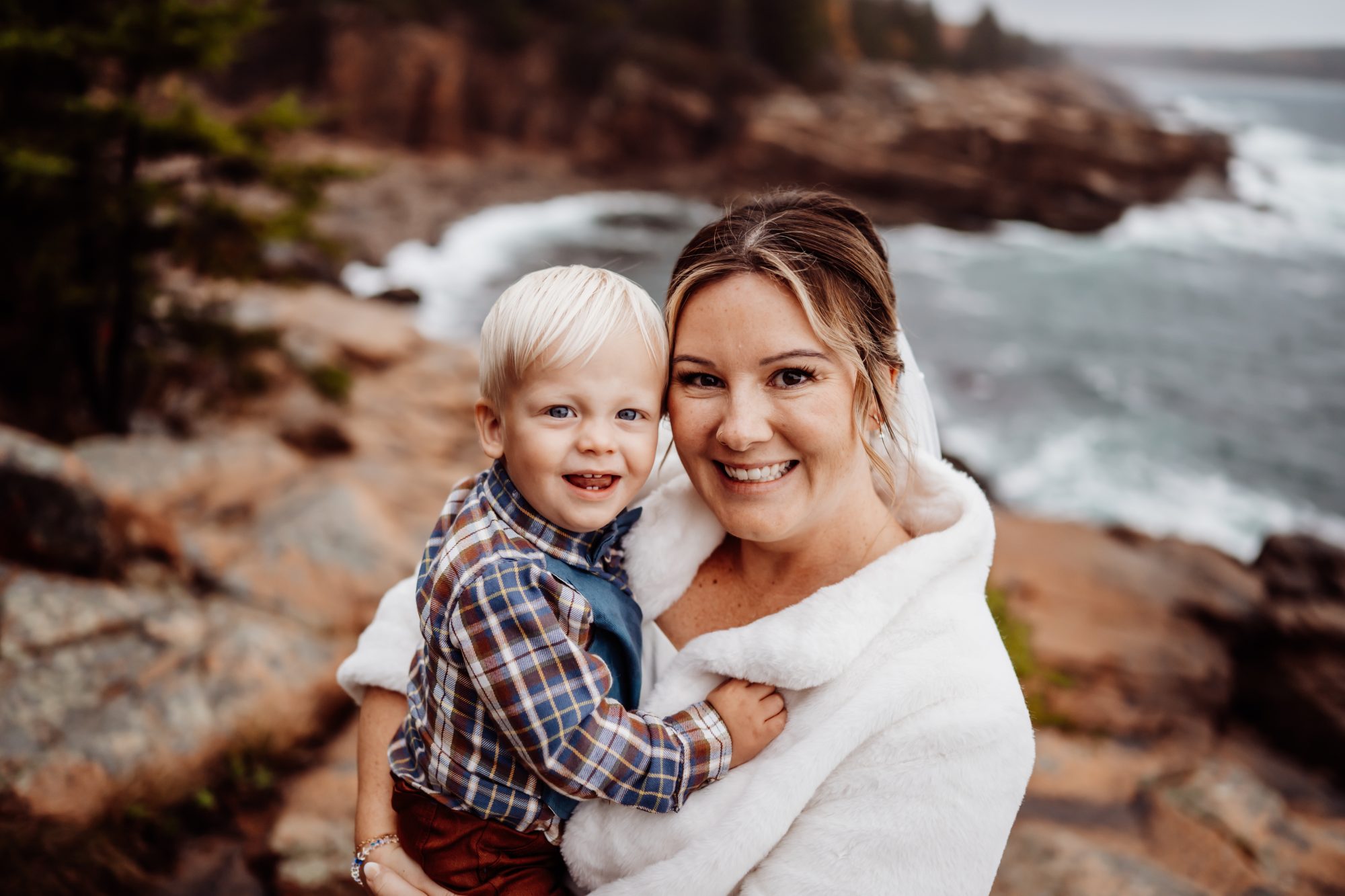 Bride holding child during intimate family moment at Thunder Hole elopement in Acadia.