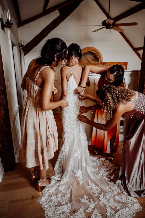 Women helping bride fasten back of wedding dress