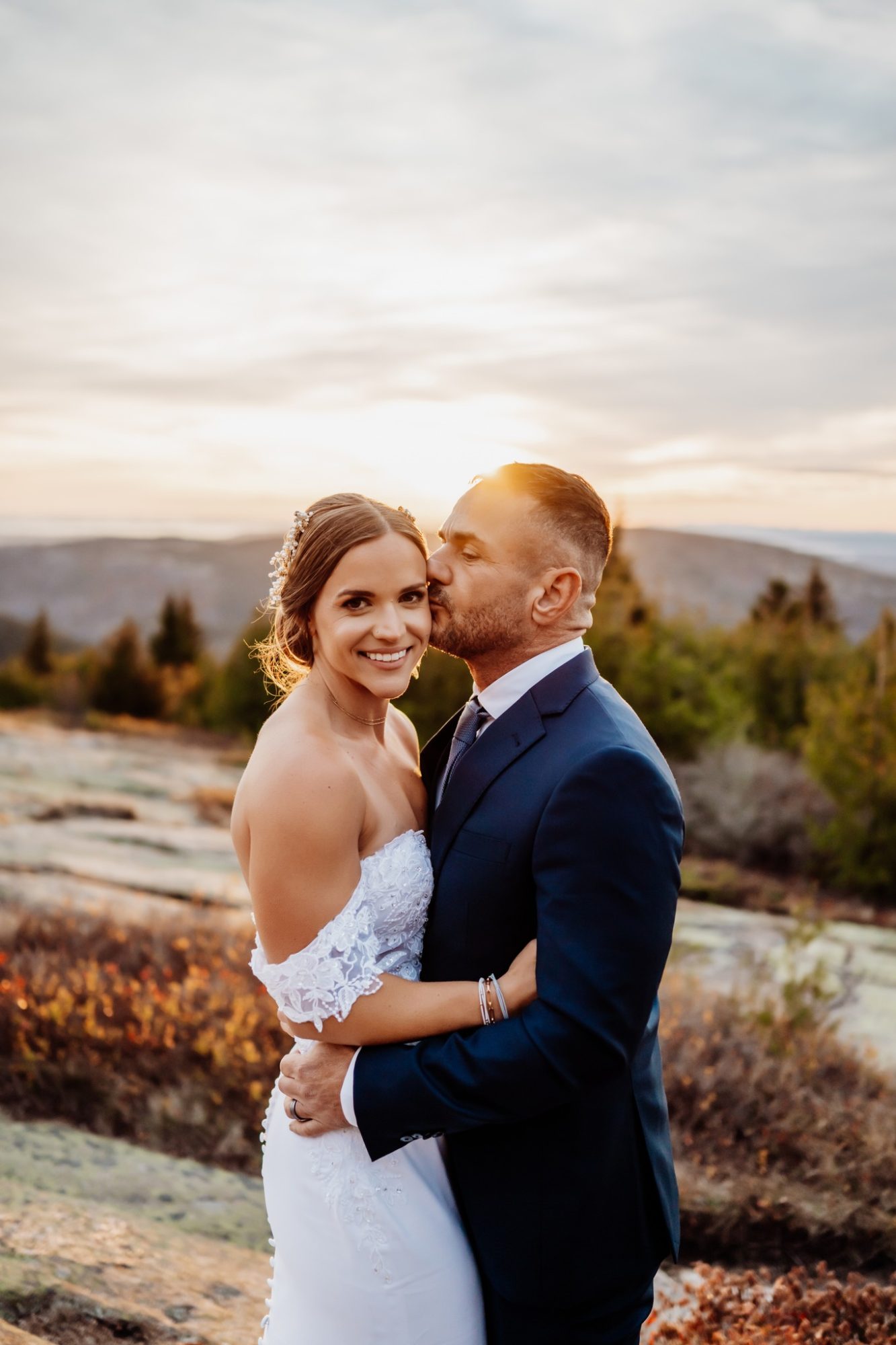 Golden hour portrait of bride and groom at Schooner Head Overlook in Acadia National Park with warm sunset light over the mountains.