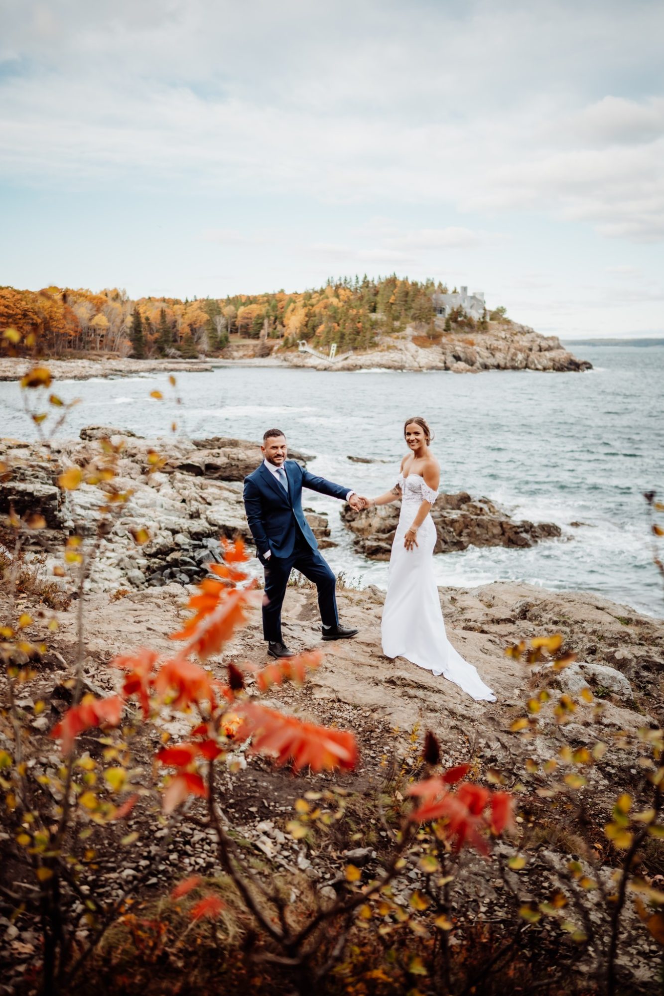 Bride and groom holding hands with fall foliage framing their Schooner Head Overlook elopement along the Acadia National Park coastline.
