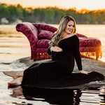 Woman wearing a black dress sitting on a rock in the lake with a chair