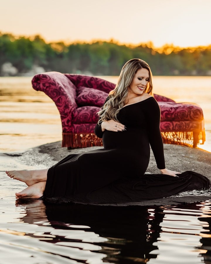 Woman wearing a black dress sitting on a rock in the lake with a chair