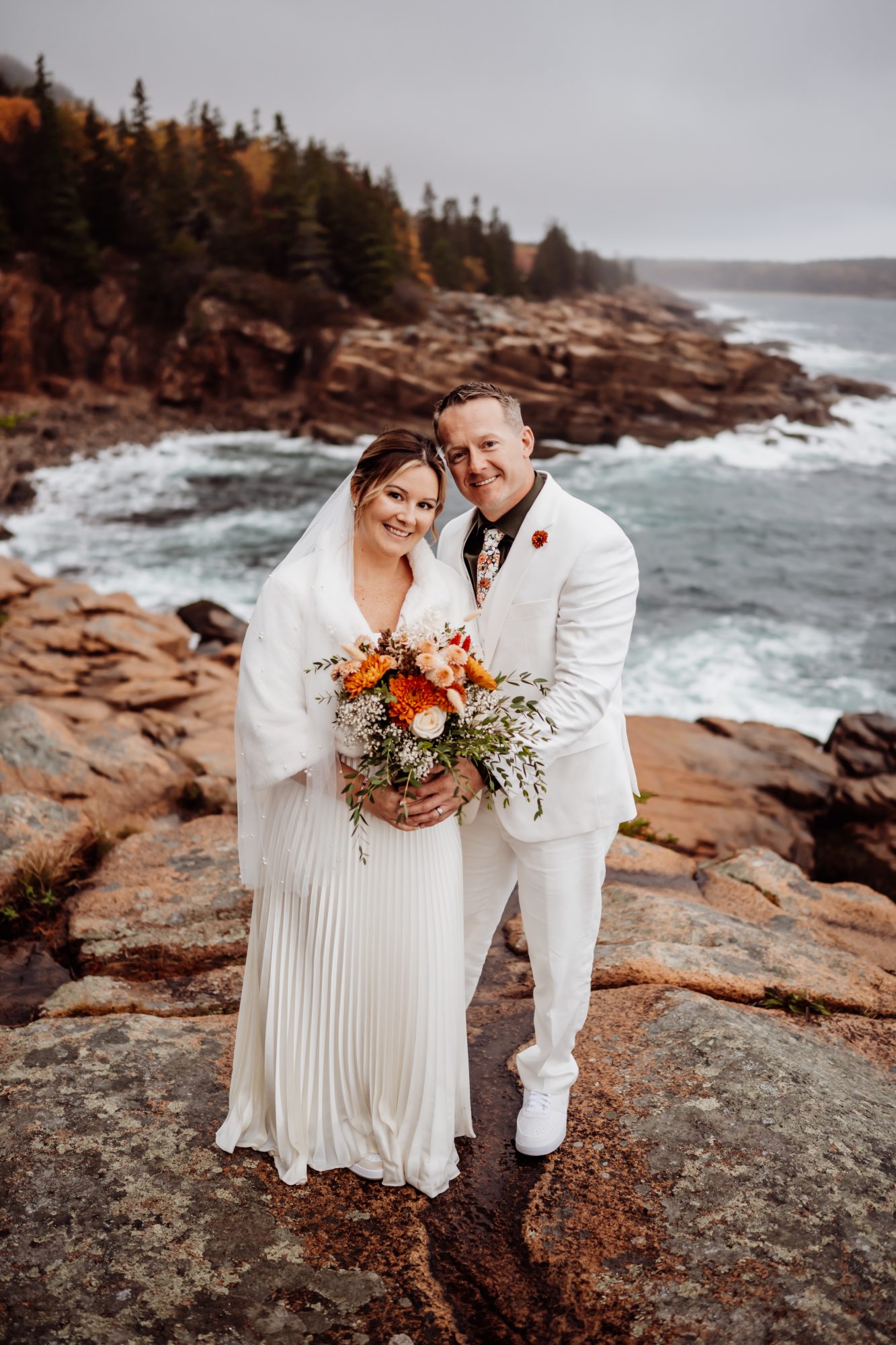 Bride and groom smiling together on granite cliffs at Thunder Hole overlooking the Atlantic.