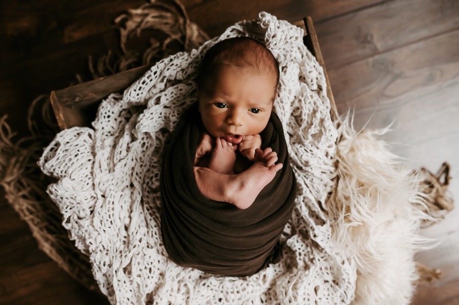 Newborn baby posed and wrapped in green looking up