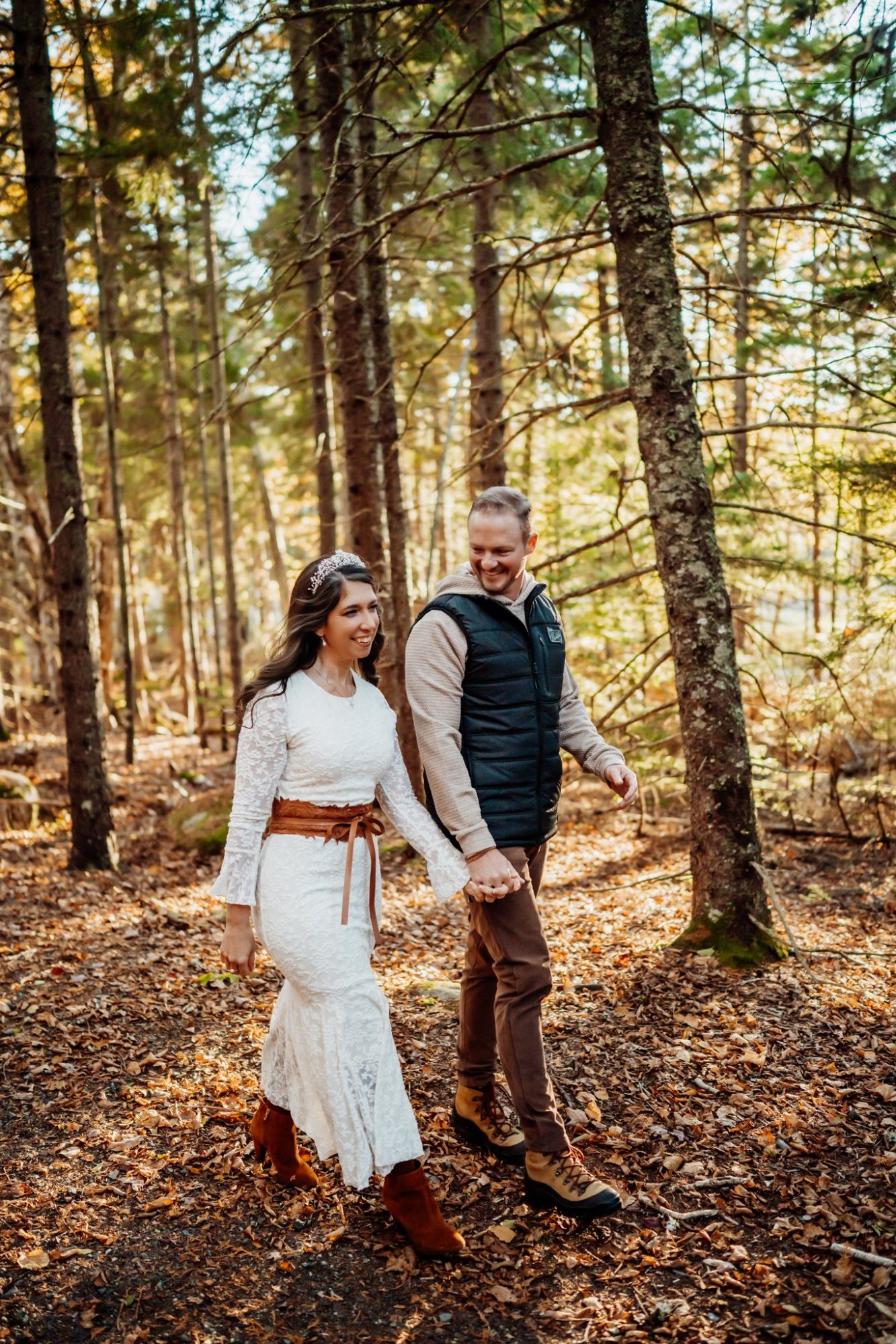 Bride and groom walking through golden forest during autumn elopement in Acadia National Park.