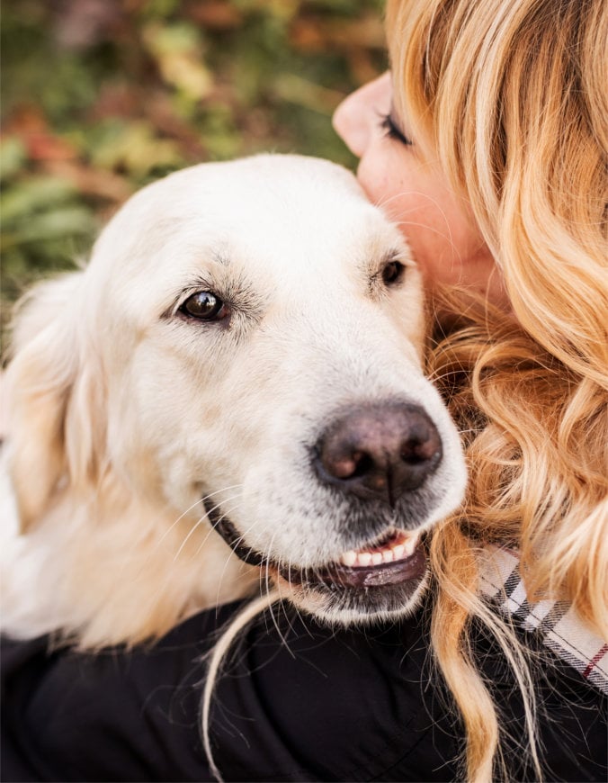 A blond woman hugging her retriever dog in the park