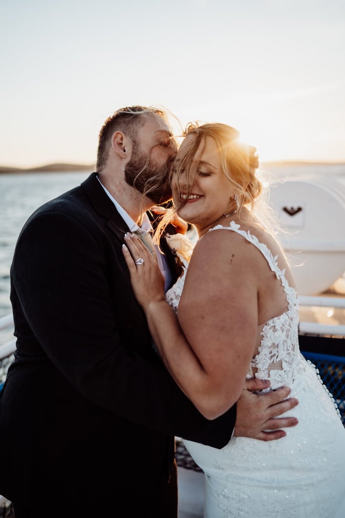 Bride and groom share a joyful embrace on a Bar Harbor sunset cruise, golden light glowing behind them as the ocean breeze lifts her hair.