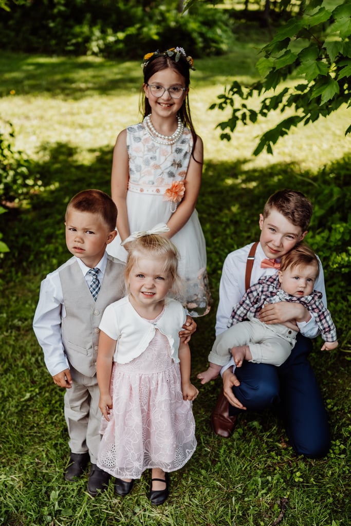 A group of children dressed for a wedding, smiling and standing outdoors in a grassy area.