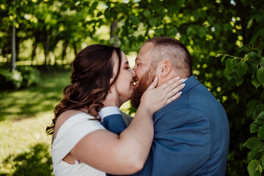 A bride and groom kissing outdoors, surrounded by lush green foliage