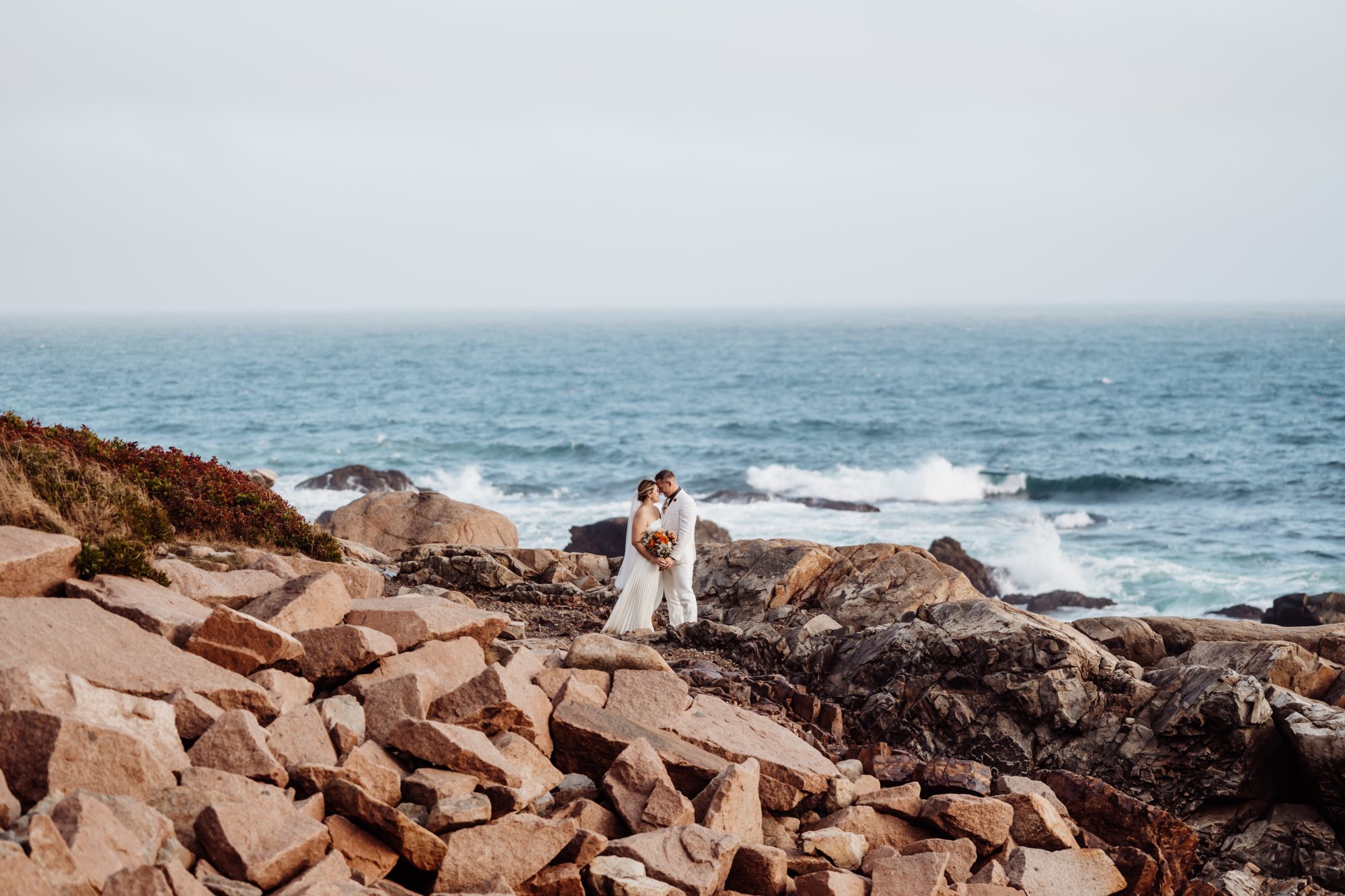 Couple embracing on rocky shoreline during intimate Thunder Hole elopement.