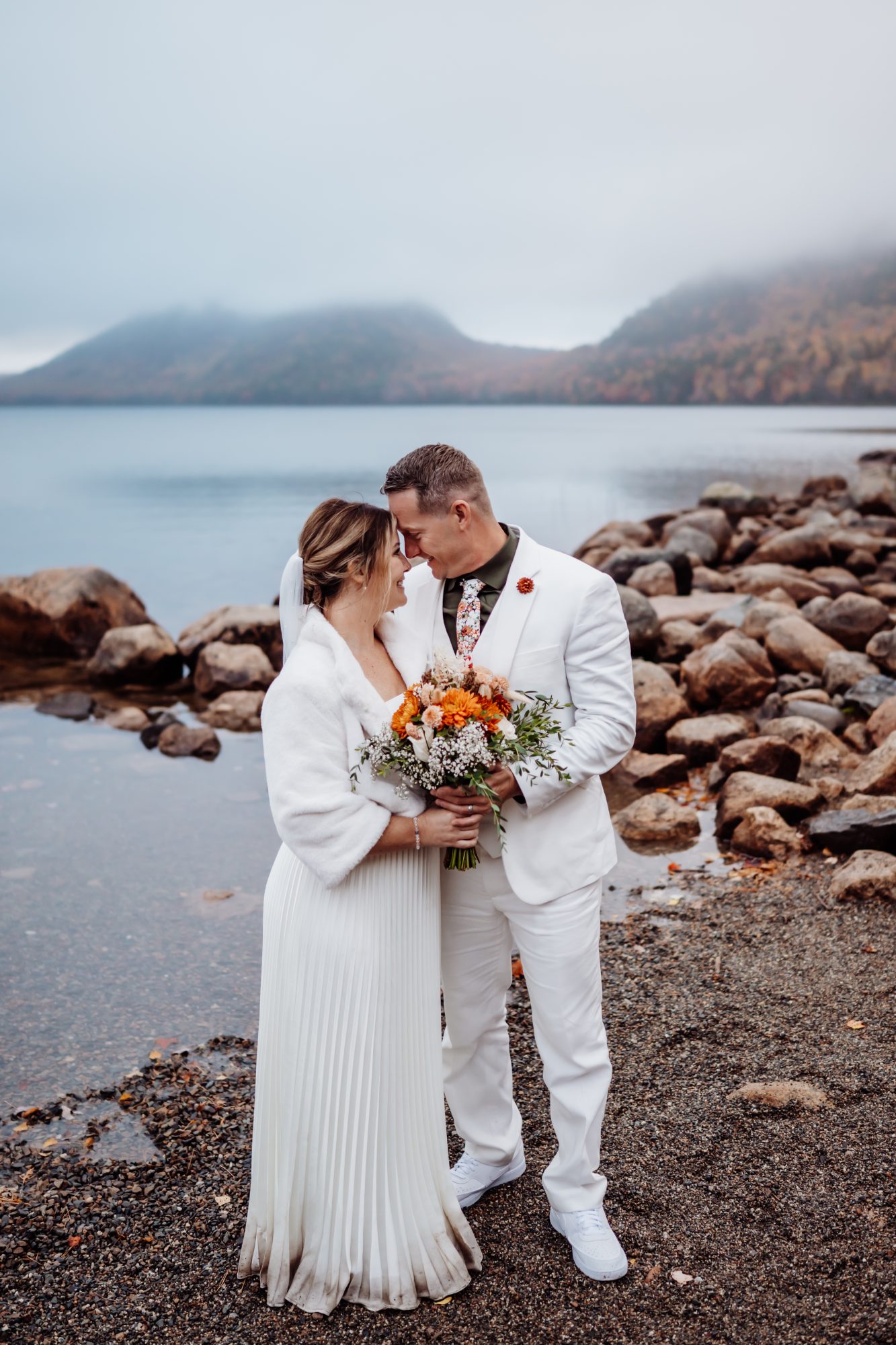 Newly married couple holding bouquet along Jordan Pond shoreline in Acadia.