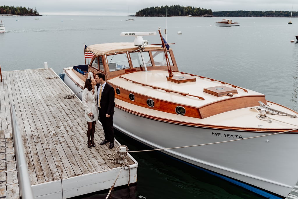 Bride and groom standing on dock kissing in front of Jericho boat