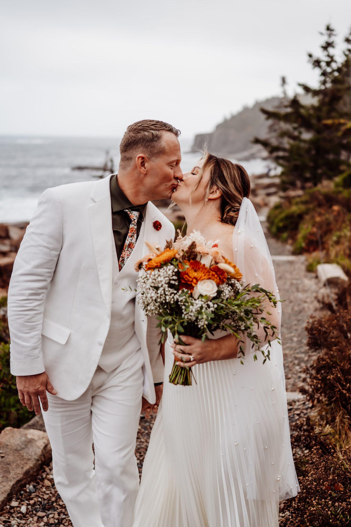 Bride and groom kissing at Thunder Hole in Acadia National Park with dramatic coastal cliffs and ocean waves behind them.