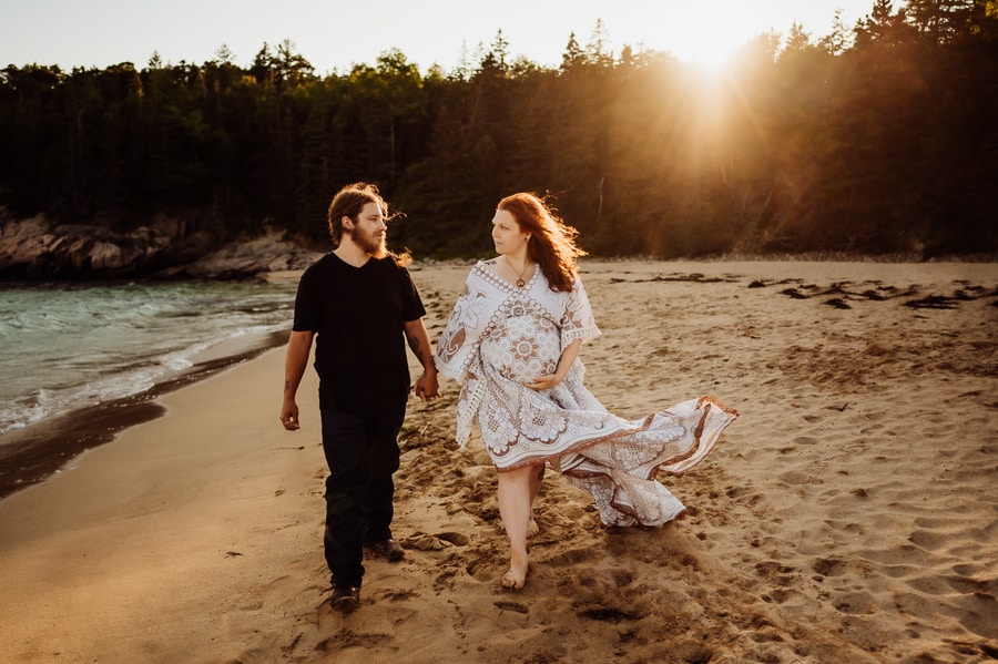 couple walking on sand beach for maternity photos