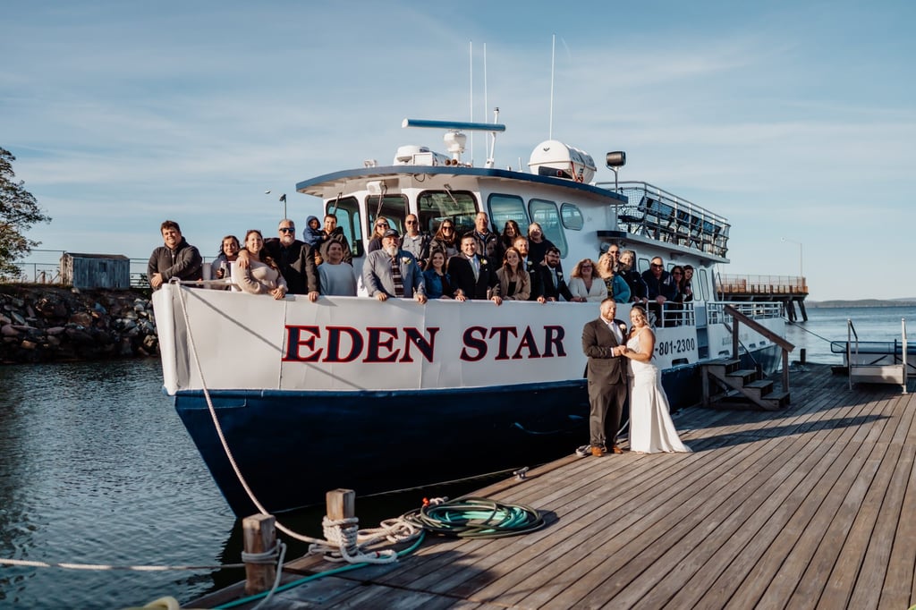 Bride and groom standing on the dock in front of the Eden Star charter boat with their wedding guests gathered on board, celebrating a Bar Harbor coastal wedding cruise in Maine.