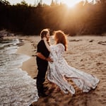 Pregnant woman and husband on sand beach in white dress