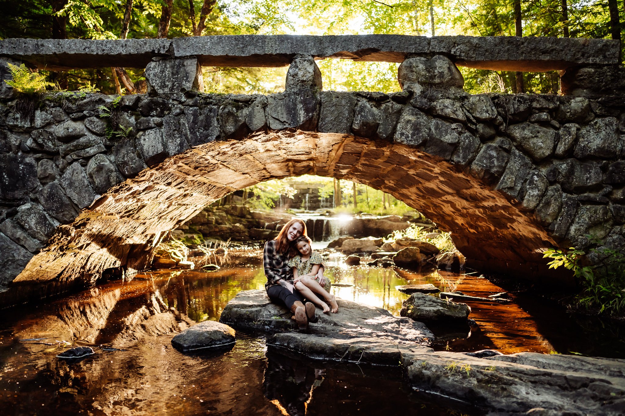 Mother and daughter sitting on rock underneath a car will Stonebridge