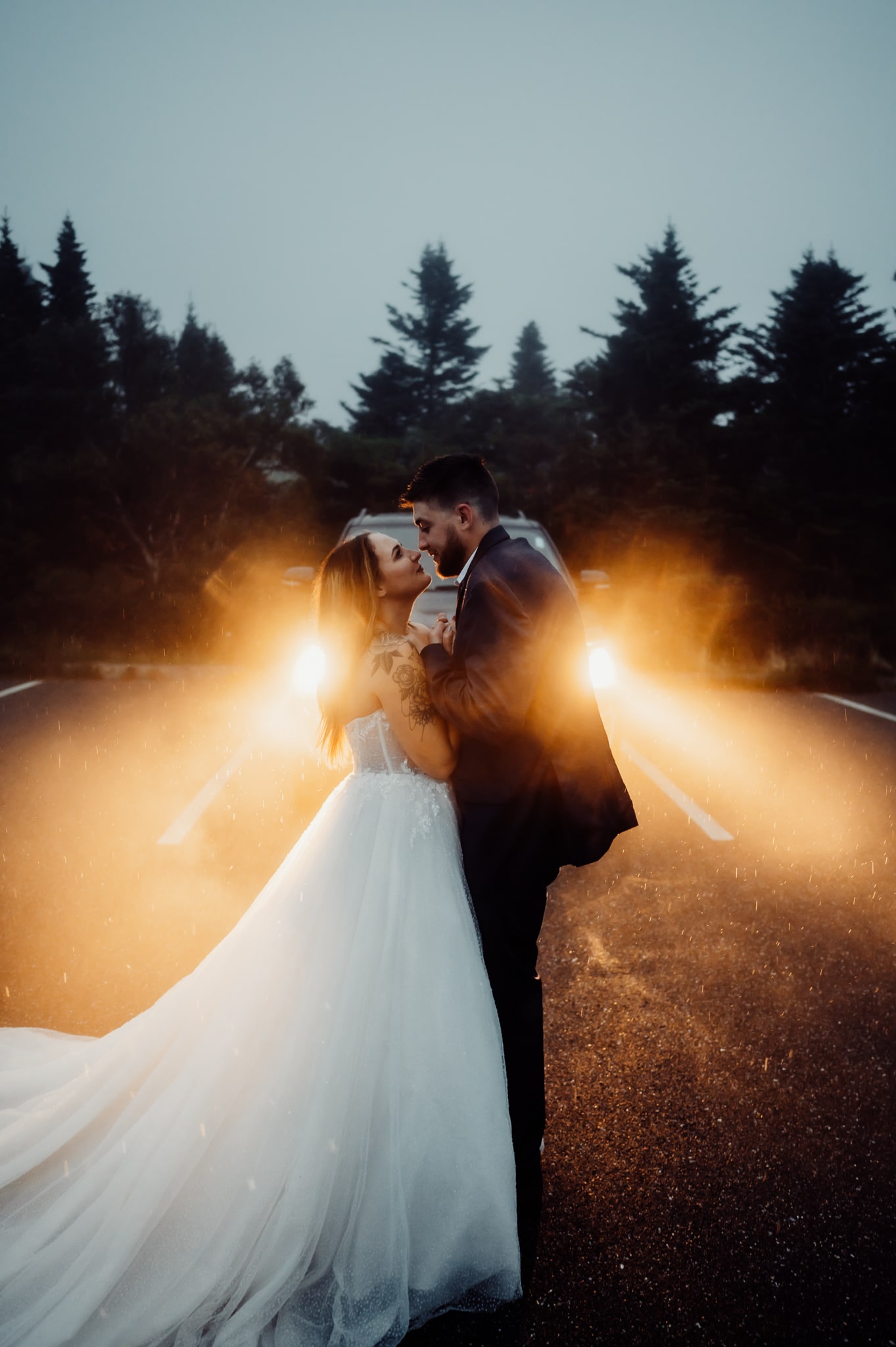 And groom standing in the rain in front of car headlights