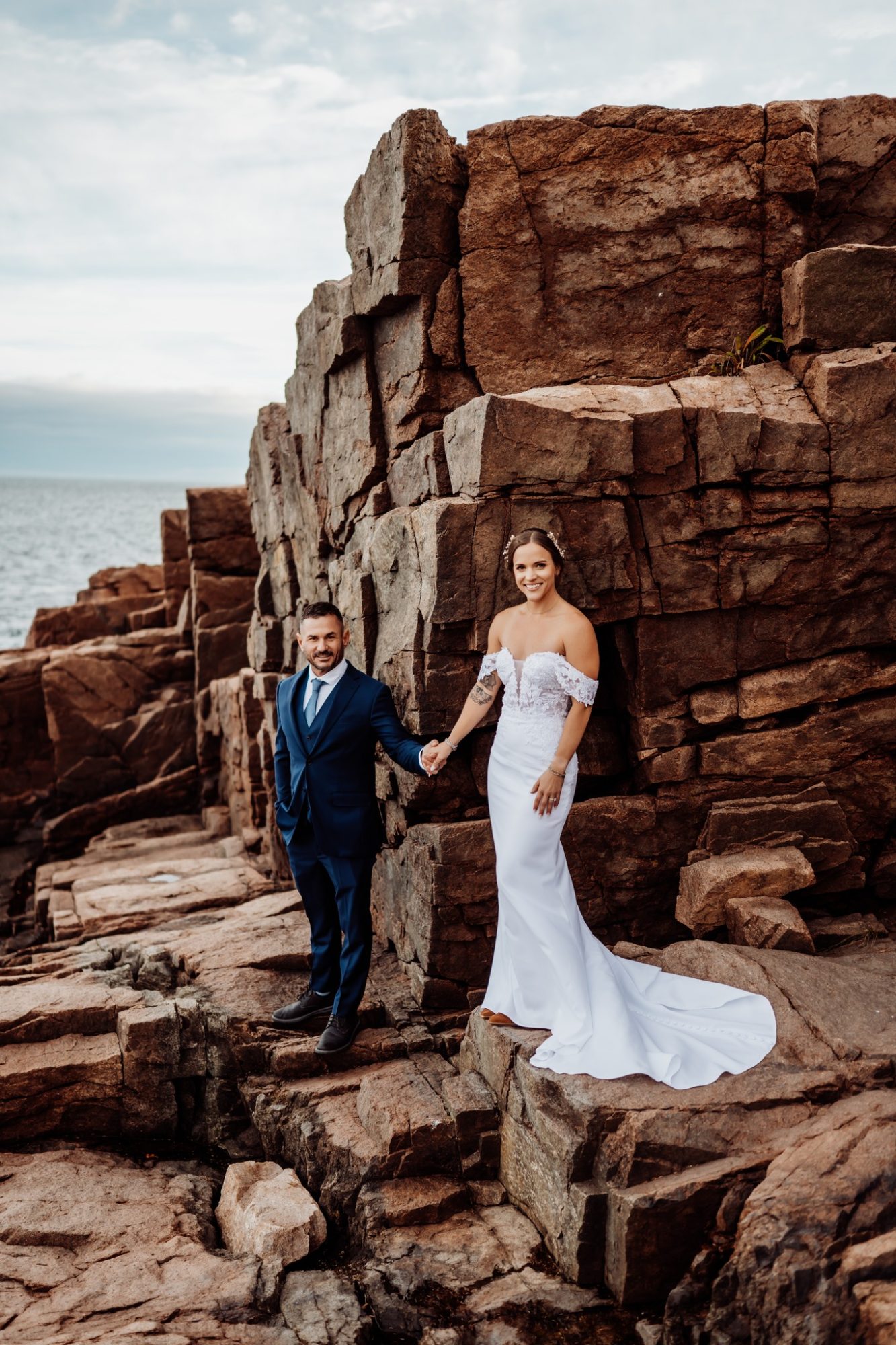 Bride and groom walking near dramatic red granite cliffs at Schooner Head in Acadia National Park.