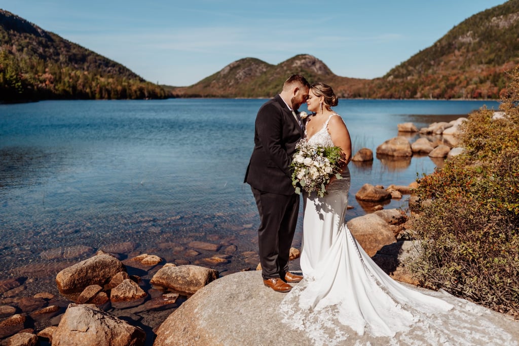 Bride and groom standing on a rock by Jordan Pond in Acadia National Park with the Bubbles mountains in the background.