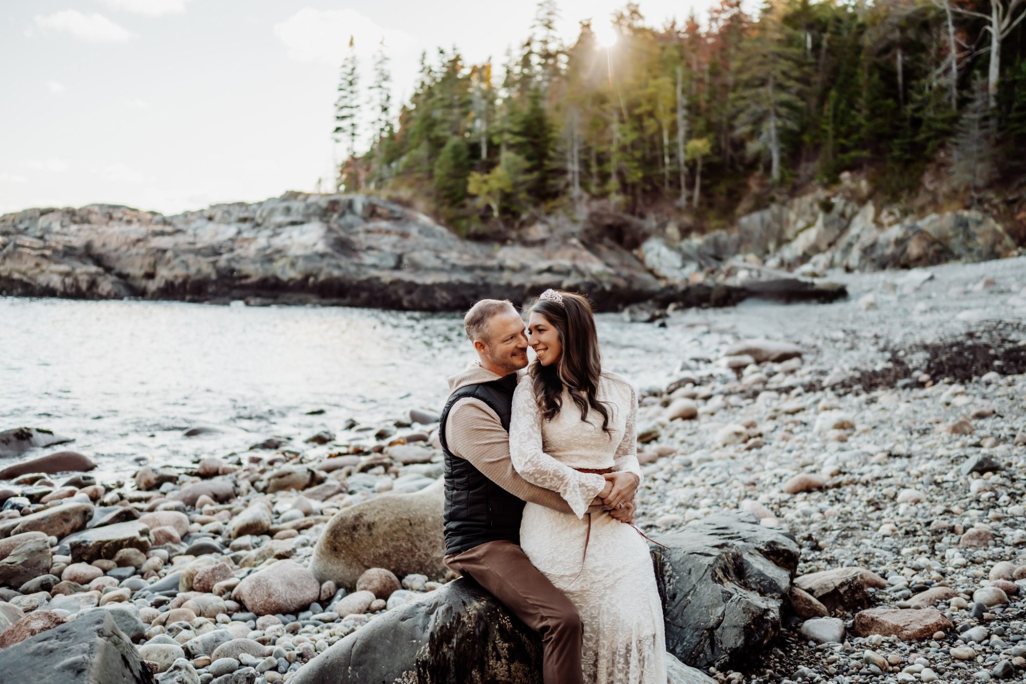 Newly married couple sitting on rocky shoreline during fall elopement in Acadia.