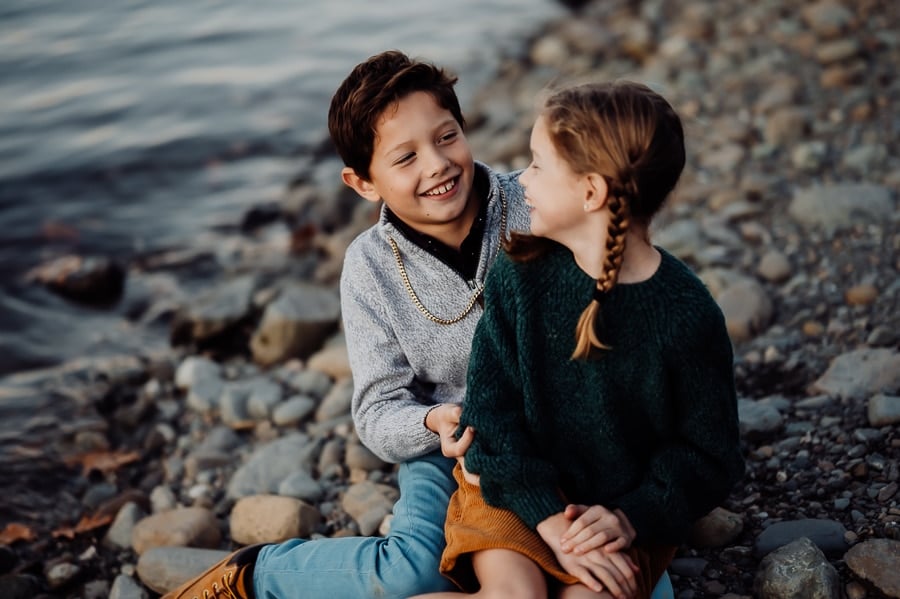 Girl sitting on boys lap at beach looking at each other