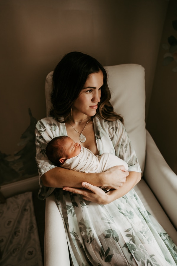 Mother holding newborn looking out window in chair