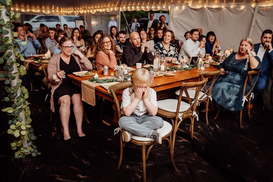 Little boy sitting in chair at tables crying at wedding reception speeches