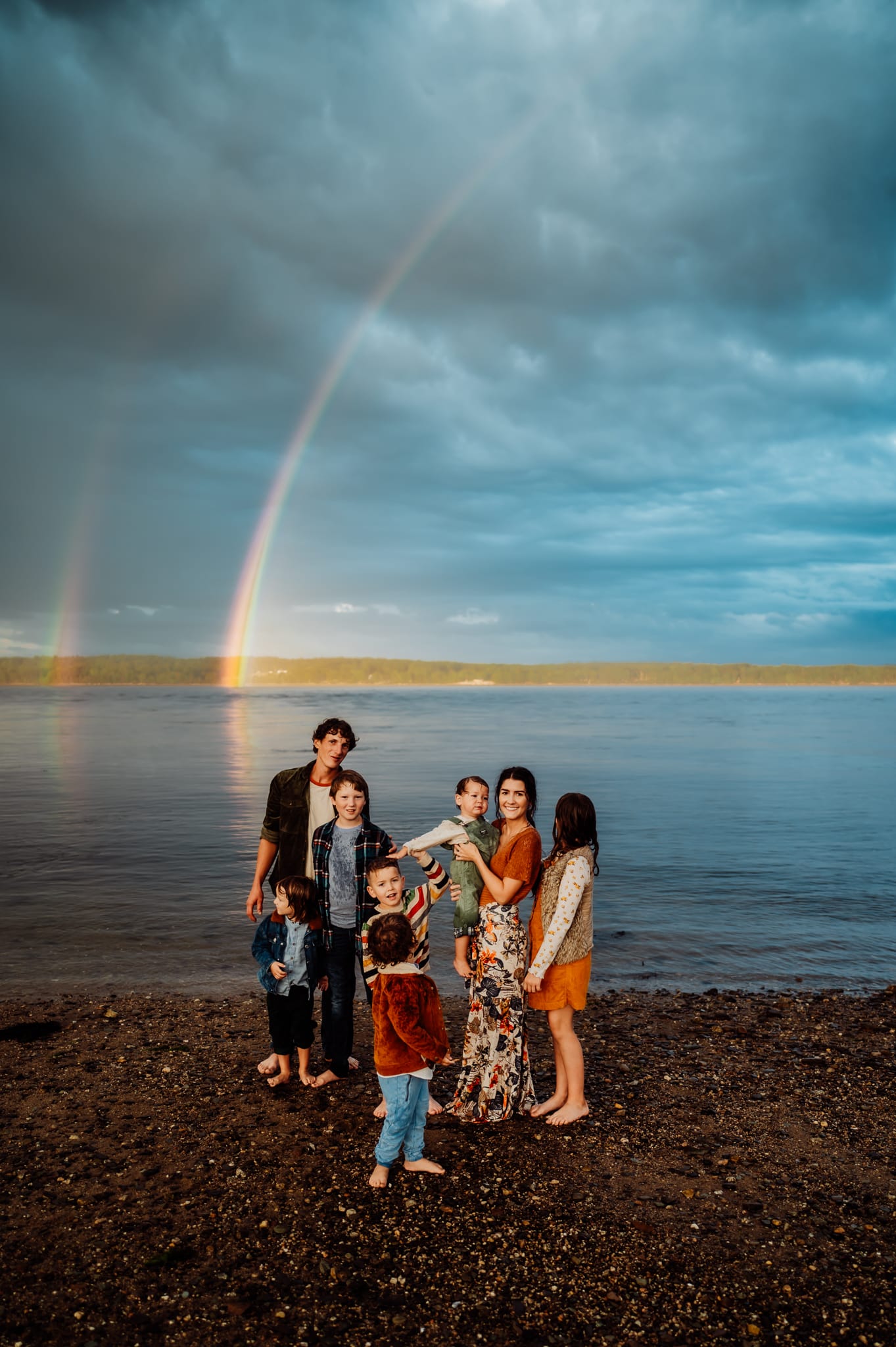 Big family with lots of kids in front of water with dark clouds and rainbows